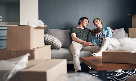 Couple sitting on couch while moving into their new home. Promo: Home Loans