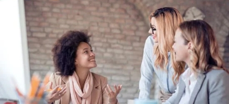 Three business women in conversation at a desk. 