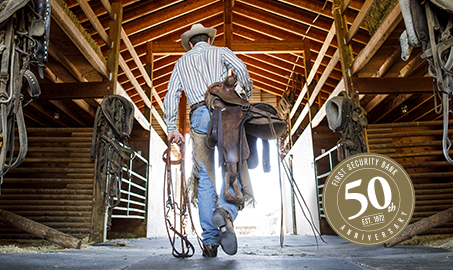 photo of cowboy carrying saddle through barn